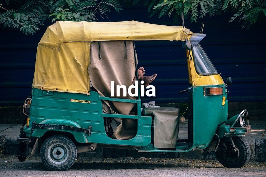 Green and yellow tuk tuk with a man sleeping inside and the word India displayed as a text overlay