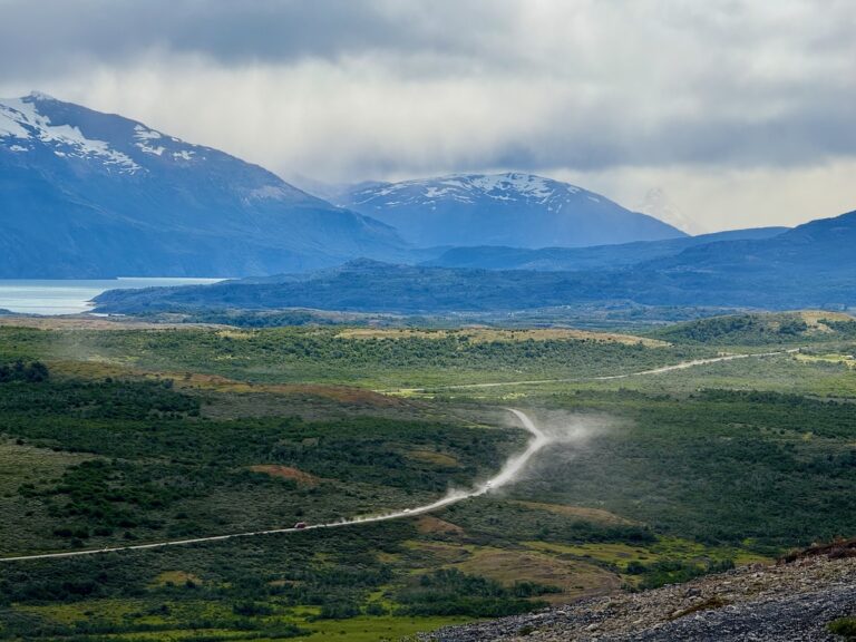 Vehicle raising dust on a winding gravel road through the mountains near Puerto Natales