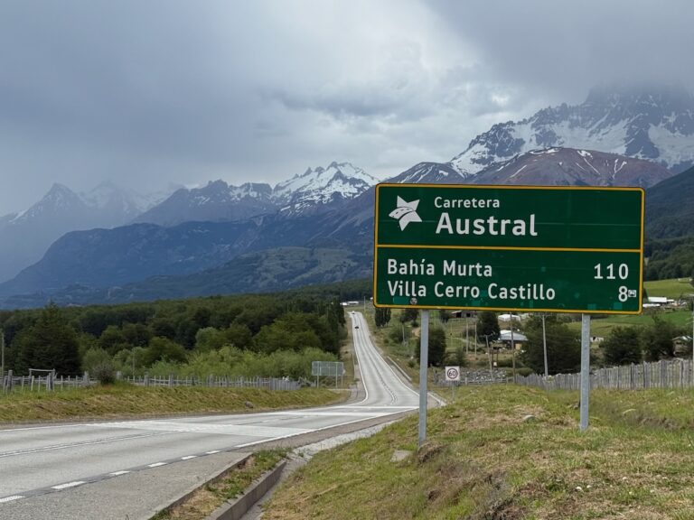 Carretera Austral road sign showing 110 km to Bahía Murta and 8 km to Villa Cerro Castillo, backed by snow-covered mountains
